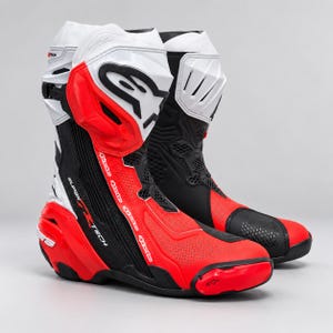 Puede incluir: Un par de botas de carreras de motos Alpinestars Supertech en una combinación de colores rojo, blanco y negro. Las botas presentan un diseño de corte alto con paneles protectores de plástico moldeado, secciones perforadas y el logo.