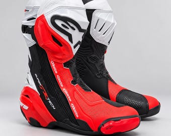 Può includere: Un paio di stivali da corsa per moto Alpinestars Supertech in una colorazione rossa, bianca e nera. Gli stivali presentano un design a taglio alto con pannelli protettivi in plastica stampata, sezioni traforate e il logo Alpinestars.