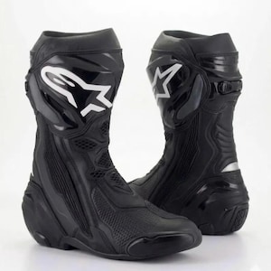 Puede incluir: Un par de botas de moto negras con diseño de caña alta, paneles de protección reforzados, detalles de malla texturizada y el logotipo blanco de Alpinestars visible en el lado exterior de la parte superior del calzado.