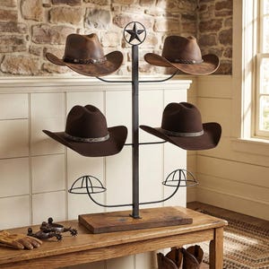 May include: A black metal hat rack with a central vertical post topped by a star, featuring four curved arms for hats and two lower wire dome supports. The rack has a rectangular wooden base and holds two distressed brown and two dark brown hats.