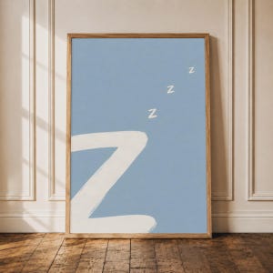 May include: A rectangular wall art print in a wooden frame featuring a light blue background with a large, white, hand-painted letter Z in the lower left corner and three smaller white Zs floating diagonally above it to represent sleeping.