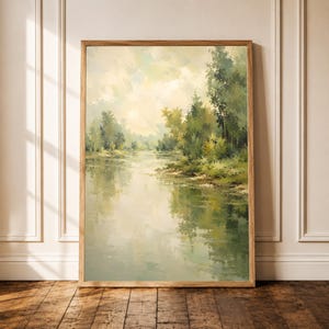 Può includere: Una stampa artistica da parete rettangolare verticale che raffigura un dipinto paesaggistico impressionista di un fiume calmo che scorre accanto a una foresta verdeggiante sotto un cielo soffuso e nebbioso, in una cornice di legno chiaro.