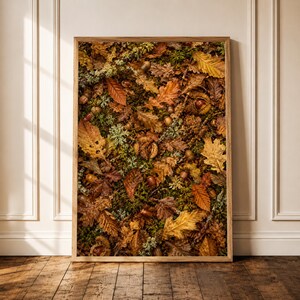 Könnte beinhalten: Ein rechteckiger gerahmter Wandkunstdruck mit einer Draufsicht auf einen Waldboden, der mit einer dichten Schicht gefallener Herbstblätter in Braun-, Orange- und Gelbtönen bedeckt ist, durchsetzt mit grünen Moosflecken und kleinen Eicheln.