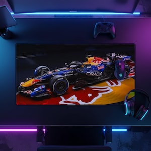 May include: A rectangular desk mat featuring a high-resolution graphic of a dark blue and yellow Oracle Red Bull Racing Formula 1 car. The design includes the Red Bull logo, the text Oracle, Carlyle, and ROKT, set against a red and yellow background.