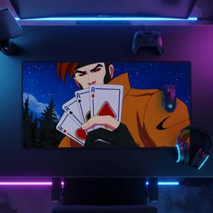 Può includere: Un tappetino da scrivania rettangolare con un'illustrazione grafica di un personaggio con occhi rossi e capelli castani che tiene in mano tre carte da gioco, tra cui un asso di quadri, su un cielo notturno blu scuro con alberi e una giacca giallo-arancio.