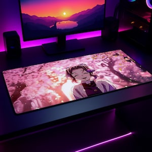 Op de afbeelding: Een rechthoekige bureaumat met een geprinte anime-illustratie van een lachend personage met donker haar en een vlinderhaaraccessoire, tegen een achtergrond van roze kersenbloesembomen met vallende bloemblaadjes in een zacht, levendig kleurenpalet.