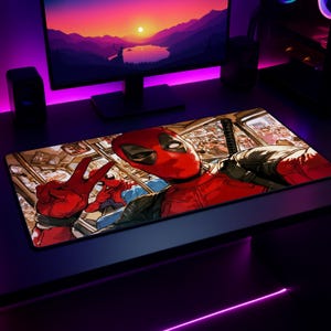 May include: A rectangular desk mat featuring a vibrant comic book illustration of Deadpool taking a selfie with a peace sign gesture, with Spider-Man visible in the background, set against a detailed urban bus interior scene with bold red tones.