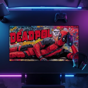Può includere: Un tappetino da scrivania rettangolare con un'illustrazione grafica del personaggio Deadpool sdraiato. Lo sfondo mostra un collage colorato in stile graffiti con il testo DEADPOL in grandi lettere rosse. Il tappetino è posizionato su una scrivania scura.