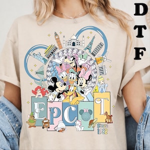 May include: A beige t-shirt featuring a graphic print of Disney characters including Mickey Mouse, Minnie Mouse, Donald Duck, Daisy Duck, Goofy, and Pluto in front of the Epcot geodesic sphere, surrounded by world landmarks and the text EPCOT Since 1982.