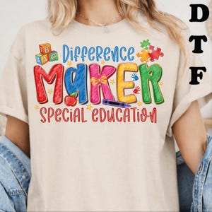 May include: A beige t-shirt featuring a colorful graphic with the text "Difference MAKER SPECIAL EDUCATION". The design includes alphabet blocks, a red apple, a yellow bow, a purple crayon, puzzle pieces, and handprints in various bright colors.