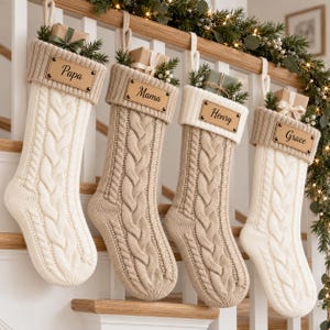 Puede incluir: Cuatro calcetines navideños de punto trenzado en tonos crema y beige, cada uno con una etiqueta de cuero personalizada con los nombres Papa, Mama, Henry o Grace. Cada calcetín está decorado con un pequeño regalo envuelto y vegetación.