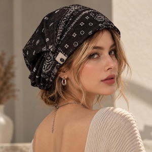 May include: A black head covering featuring a white bandana-style print with various small geometric and floral patterns. The fabric is gathered at the back and includes a small white rectangular tag with a single black button on the side.