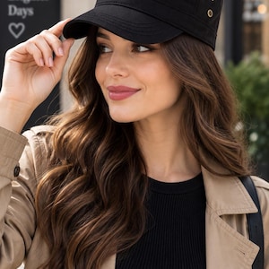 May include: A black military-style cadet cap featuring a flat top, a curved brim, and two small metallic eyelets on the side. The cap is constructed with horizontal stitched detailing along the crown and a structured band around the base.