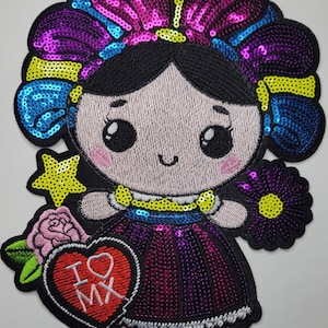 May include: A sequined embroidered patch featuring a cartoon doll with black hair, a purple and blue headpiece, and a dark purple dress. The doll holds a red heart-shaped sign with the white text I heart MX, a pink rose, and a purple flower.