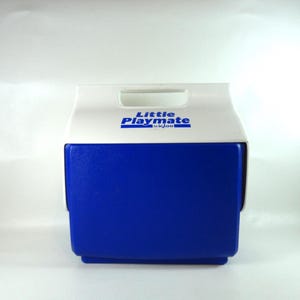 Puede incluir: Nevera portátil Little Playmate Igloo azul y blanca. La nevera tiene una tapa blanca con asa y las palabras "Little Playmate by Igloo" en azul. El cuerpo de la nevera es de color azul liso.