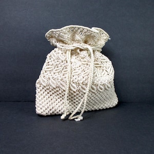 May include: Off-white macrame drawstring bag. The bag features a textured, open weave design with a cinched top and matching drawstring closure. The bag is made of a soft, natural fiber and is suitable for carrying small items.