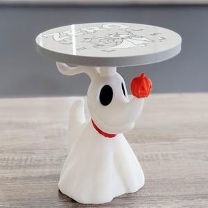 May include: A white ghost dog figurine with a red collar and a small orange pumpkin on its nose, supporting a round white tabletop. The tabletop features a black graphic illustration of a ghost dog, the text ZERO, and the year 1993.