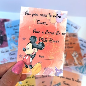Puede incluir: Una tarjeta rectangular con fondo de acuarela naranja que muestra a Mickey Mouse con pantalones cortos rojos y zapatos amarillos. El texto dice: All you need is faith trust... AND A LITTLE BIT OF PIXIE DUST. Incluye una línea From y globos.
