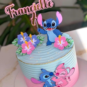 Op de afbeelding: Een ronde taart met lichtblauw en roze glazuur, versierd met een blauwe Stitch-figuur, een roze Angel-personage en hibiscusbloemen. Een roze acryl taarttopper toont de naam Francielle en het cijfer 7 in een sierlijk lettertype.