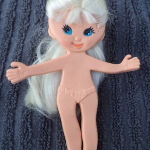 Puede incluir: Una muñeca de plástico con el pelo largo y rubio, ojos azules y cuerpo rosa. La muñeca lleva una parte inferior de bikini rosa.