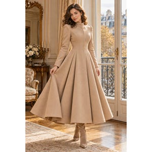 May include: A long-sleeved, floor-length beige coat dress featuring a high mock neck, a fitted bodice, and a full, pleated skirt that flares out from the waist. The garment is crafted from a solid-colored fabric and includes matching beige boots.