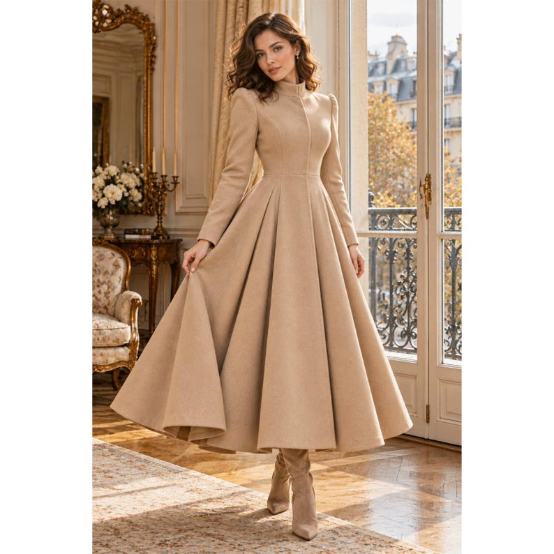 May include: A long-sleeved, floor-length beige coat dress featuring a high mock neck, a fitted bodice, and a full, pleated skirt that flares out from the waist. The garment is crafted from a solid-colored fabric and includes matching beige boots.