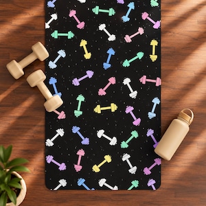 Puede incluir: Una esterilla de ejercicio rectangular con fondo negro y un patrón repetitivo de mancuernas en tonos pastel de rosa, azul, amarillo, verde, morado y blanco, acompañada de dos mancuernas beige y una botella de agua beige.