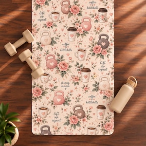 May include: A rectangular yoga mat featuring a repeating pattern of pink roses, kettlebells, and coffee cups with hearts. The text reads lift sip repeat, coffee n kettlebells, and strong mama. Two beige dumbbells and a beige water bottle are present.