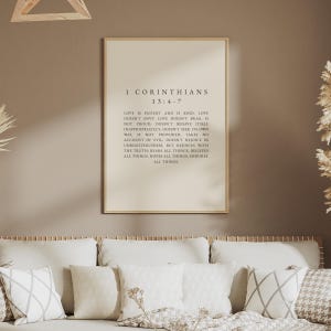 May include: A rectangular wall art print in a light wood frame featuring the text of 1 Corinthians 13:4-7 in black serif font on a cream background. The passage reads: Love is patient and is kind. Love doesn't envy. Love doesn't brag.
