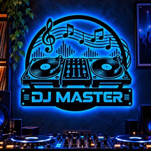 May include: A black wall sign with bright blue LED backlighting featuring a graphic of two turntables, a mixer, musical notes, and a treble clef. The text DJ MASTER is displayed in a bold, sans-serif font at the bottom of the sign.