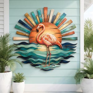 May include: A circular wall art piece featuring a pink flamingo standing in teal and blue waves. Behind the flamingo is a large orange sun with radiating wooden slats in shades of orange, teal, and blue, creating a sunset scene.