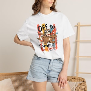 May include: A white short-sleeve t-shirt featuring a graphic of a cat wearing aviator goggles and a red scarf, flying a brown cardboard airplane. The text reads Off to Commit tomfoolery, set against vertical stripes of orange, blue, and red colors.