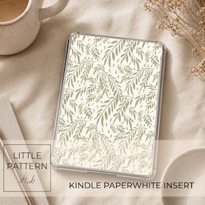Puede incluir: Un inserto rectangular para Kindle Paperwhite con un patrón botánico repetitivo de hojas de sauce de color verde salvia sobre un fondo crema, encerrado en una funda protectora transparente con una superficie lisa y esquinas redondeadas.