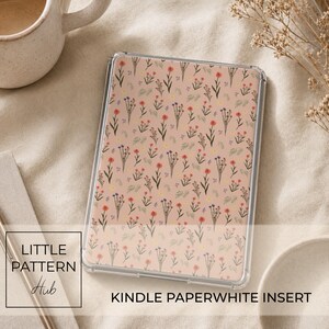 Pode incluir: Uma inserção retangular para Kindle Paperwhite com um padrão repetitivo de pequenas flores silvestres vermelhas, roxas e amarelas sobre um fundo pêssego suave. A inserção está protegida por uma capa transparente com um design botânico.