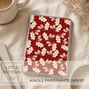 May include: A rectangular Kindle paperwhite insert featuring a repeating pattern of cream-coloured oak leaves and acorns set against a deep burgundy red background. The insert is encased in a clear protective cover with a smooth, glossy finish.