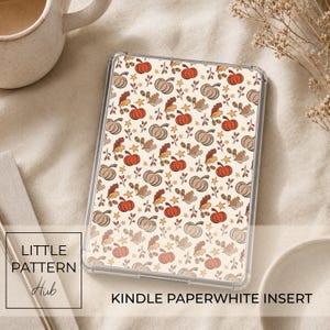 Może przedstawiać: Przezroczyste etui ochronne na czytnik Kindle Paperwhite z ozdobną wkładką w powtarzający się wzór pomarańczowych dyń, brązowych liści dębu, żołędzi i małych żółtych gwiazdek na kremowym tle. Napis na grafice brzmi LITTLE PATTERN Hub.