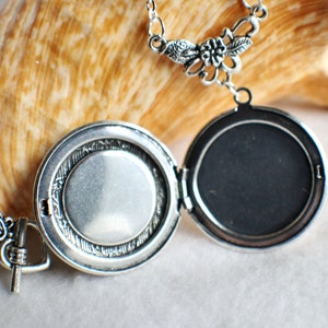 May include: Silver locket necklace with a floral design. The locket opens to reveal a blank space for a photo or message.