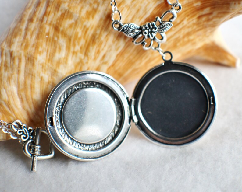 May include: Silver locket necklace with a floral design. The locket opens to reveal a blank space for a photo or message.