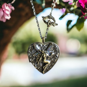 May include: A silver heart-shaped locket necklace with a detailed fairy design. The fairy is depicted with wings and a flowing dress. The necklace is hanging from a silver chain.