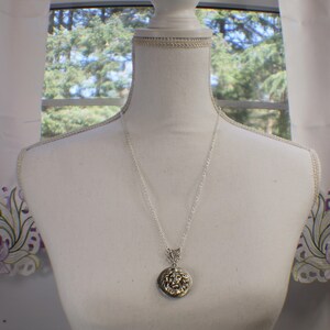 May include: A silver chain necklace with a round locket pendant featuring a detailed lion head design.