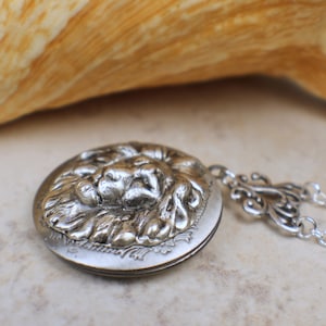 May include: Silver locket necklace with a detailed lion head design. The locket is open and the chain is silver.