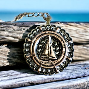 Music box locket, round bronze locket with music box inside, with a nautical theme featuring a sailboat on front cover.