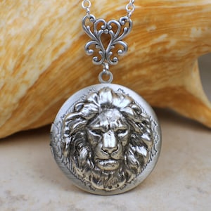 May include: Silver locket necklace with a detailed lion head design. The locket is round and has a filigree chain.