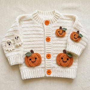 Può includere: Un cardigan all'uncinetto color crema con quattro bottoni arancioni vivaci al centro. Il capo è decorato con due zucche arancioni all'uncinetto con piccioli verdi sul davanti e una sulla manica, oltre a due piccoli fantasmi bianchi applicati.