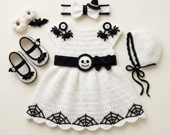 May include: A white crochet dress featuring a black waistband with a skull emblem, spider motifs on the shoulders, and a spiderweb pattern at the hem. The set includes a matching bonnet, headband with a bow and hat, and two Mary Jane shoes.