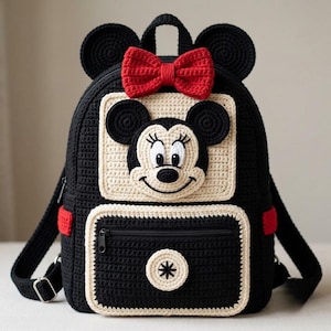 May include: A black crochet backpack featuring a cream-colored square panel with a Minnie Mouse face appliqué. The bag includes a bright red crochet bow at the top, two round black ears, and a front zippered pocket with a circular cream accent.