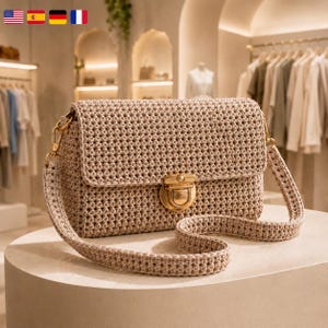 May include: A beige crochet shoulder bag featuring a rectangular flap, a textured woven pattern, and a gold-toned metal push-lock closure. The bag includes a matching crochet strap attached with gold-toned metal swivel clasps on both sides.