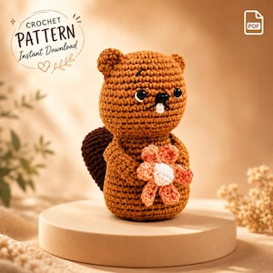 May include: A brown crochet beaver amigurumi toy holding a small peach and white flower. The beaver has black bead eyes, a black stitched nose, and a single white tooth. A dark brown tail is visible behind the body. Text reads CROCHET PATTERN.