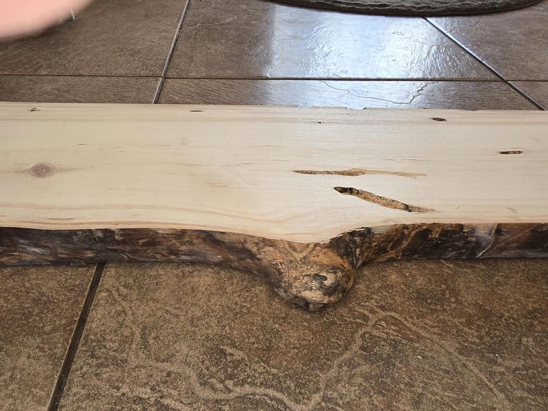 Pu&ograve; includere: Una lastra di legno naturale con un bordo vivo e un colore marrone chiaro. La lastra ha alcuni nodi e una texture ruvida.