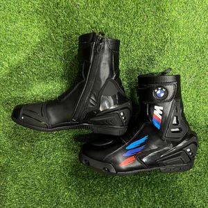 Puede incluir: Un par de botas de moto negras con cremallera lateral, protecci&oacute;n reforzada en el tal&oacute;n y el tobillo, y el logotipo de BMW. Las botas presentan rayas gr&aacute;ficas azules, moradas y rojas en el lateral e incluyen un cierre de correa en la parte superior.